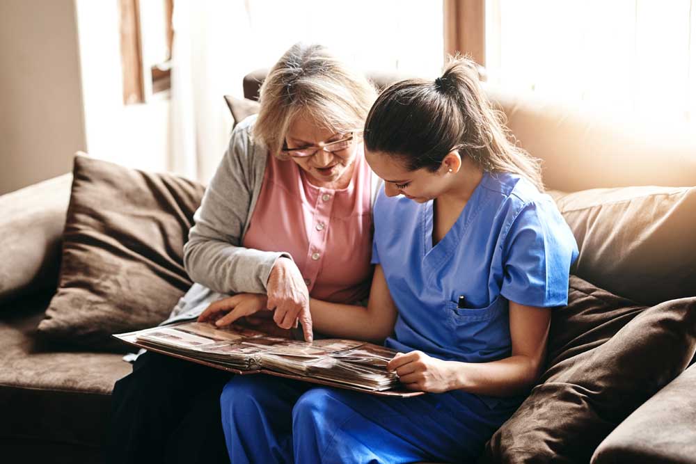 Senior woman sharing memories with a caregiver while looking through a photo album at Charter Senior Living of Newport News in Virginia.