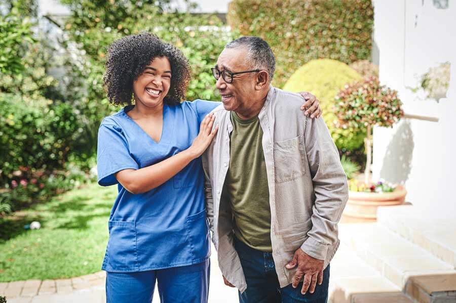 Friendly caregiver supporting a senior man during a walk outdoors at Charter Senior Living of Newport News in Virginia.