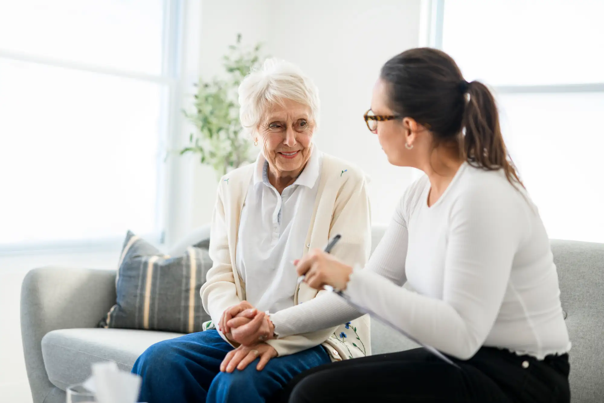 senior woman sitting on couch and holding hand of woman next to her